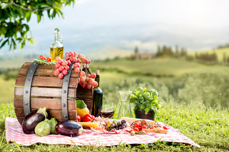 Lots of tasty italian food on the napkin and wooden barrel outdoors on the tuscany landscape backgroundの写真素材