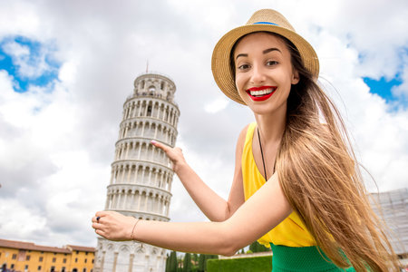 Young female traveler having fun in front of the famous leaning tower in Pisa old town in Italy. Happy vacations in Italyの写真素材