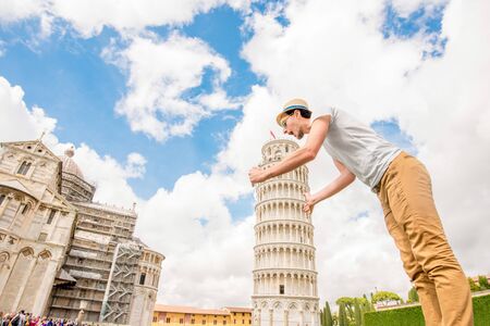 Man having fun with the famous leaning tower in Pisa old town in Italy. Happy vacations in Italyの写真素材