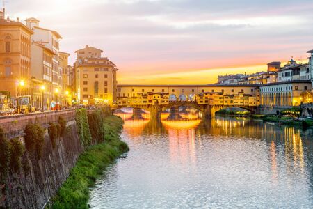 Illuminated cityscape view on Arno river with famous Ponte Vecchio bridge and buildings on the riverside on the sunset in Florenceの写真素材
