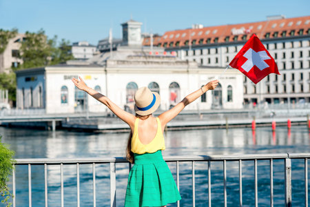 Young female traveler with swiss flag on the pedestrian bridge in the center of Geneva city in...