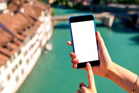 Holding a smart phone with white screen on Bern old town background in Switzerlandの写真素材