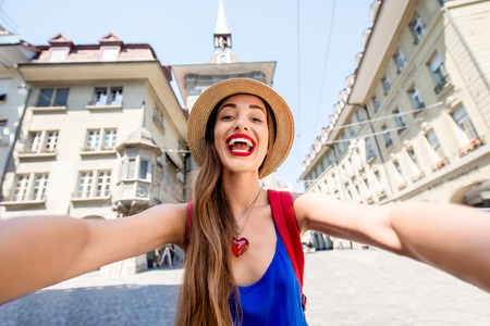 Young female tourist making selfie photo in front of the famous clock tower in the center of the old town of Bern city in Switzerland. Having a great vacations in Switzerlandの写真素材