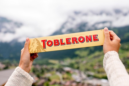 Grindelwald, Switzerland - June 26, 2016 Female hand holds Toblerone chocolate on the mountains background in Switzerland. Toblerone is a famous Swiss chocolate bar brandのeditorial素材