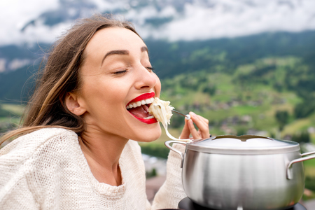 Young woman eating fondue a traditional swiss meal during a trip in the mountains in Switzerlandの写真素材