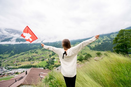 Young woman with swiss flag enjoying great view on the mountains. Having happy vacations in Switzerlandの写真素材