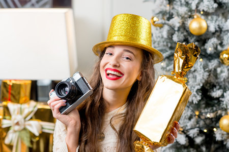 Young smiling woman in sweater and golden hat celebrating winter holidays with candy and retro...