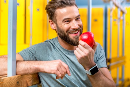 Sports man eating an apple sitting after the training in the locker room of the gym. Healthy natural food for sports menの写真素材