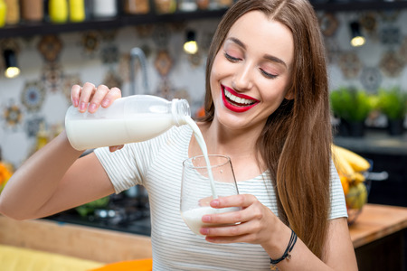 Portrait of a young smiling woman with milk in the kitchen at homeの写真素材