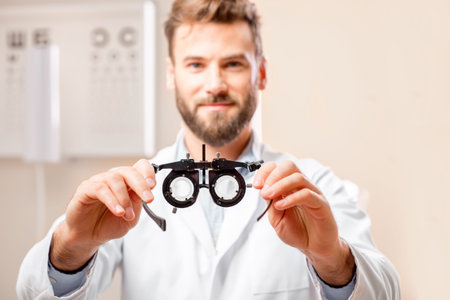 Ophthalmologist holding try-on tool for lenses selection in front of the eye chart in the cabinet....