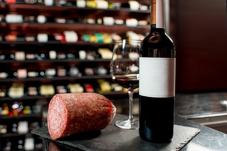 Salamy sausage with red wine on the table in the restaurant or food market. Bottle with empty label to copy pasteの写真素材