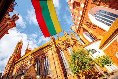View on the beautiful gothic saint Anna and Francis of Assisi churches eith lithuanian flag in the old town of Vilnius city, Lithuania.の写真素材
