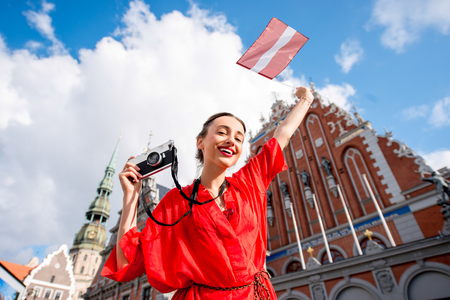 Portrait of a young female tourist with latvian flag on the main old town square in Riga. Woman having great vacations in Latviaの写真素材
