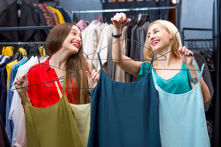 Beautiful women choosing shirts in the clothing store. Female friends having fun shopping in the boutiqueの写真素材