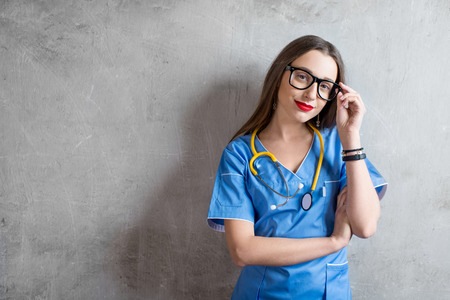 Portrait of a young nurse in uniform with stethoscope on the gray wall backgroundの写真素材
