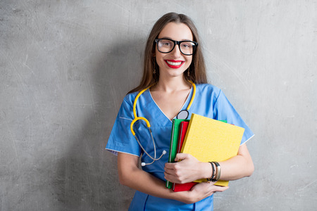 Portrait of a young nurse with colorful books and stethoscope on the gray wall backgroundの写真素材