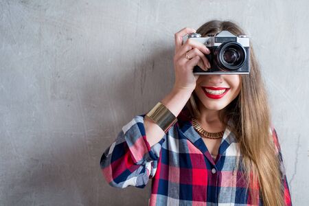 Portrait of young female photographer with retro camera on the gray wall backgroundの写真素材