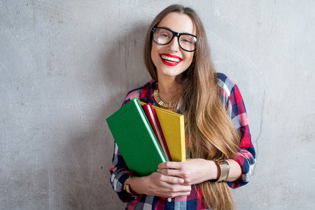 Portrait of a happy young student in checkered shirt with colorful books on the gray wall backgroundの写真素材