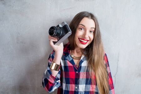 Portrait of young female photographer with retro camera on the gray wall backgroundの写真素材