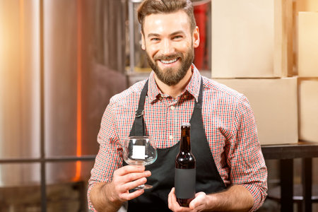 Portrait of a happy brewer holding a bottle with empty lable to copy paste at the manufacturingの写真素材