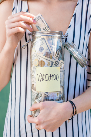 Woman holding jar full of money for summer vacationの写真素材