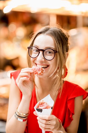 Young woman in red dress eating jamon traditional spanish dry-cured ham sitting at the Barcelona food marketの写真素材
