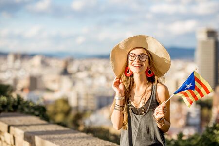 Portrait of young woman tourist sitting with catalan flag on the cityscape background in Barcelonaの写真素材