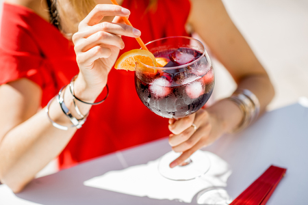 Woman holding a glass with Sangria, traditional spanish alcohol beverage made of wine, sitting outdoors at the restaurant. Image with no face focused on the glassの写真素材