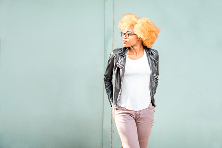 Lifestyle portrait of an african woman in leather jacket standing on the green wall backgroundの写真素材