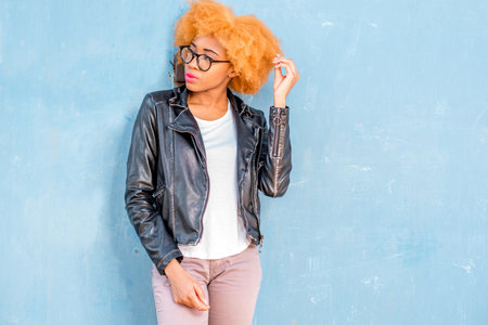 Lifestyle portrait of an african woman in leather jacket standing on the blue wall backgroundの写真素材