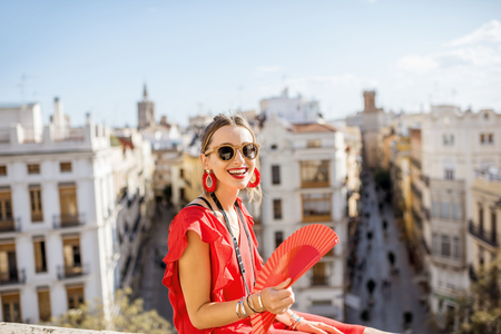 Portrait of a young woman in red dress with hand fan sitting with beautiful cityscape on the background in Valencia, Spainの写真素材