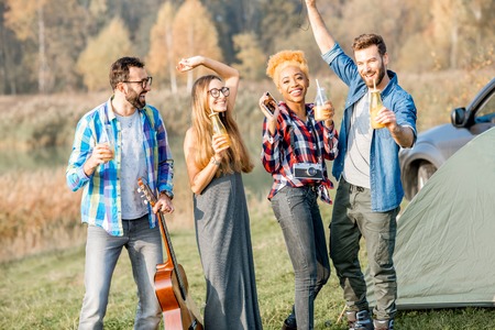 Multi ethnic group of friends dressed casually having fun dancing with drinks during the outdoor recreation at the camping near the forestの写真素材