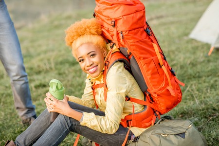 Portrait of an african woman resting with backpack and bottle outdoors on the green lawnの写真素材