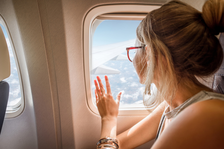 Young woman enjoying the view through the aircraft window sitting during the flight in the airplaneの写真素材