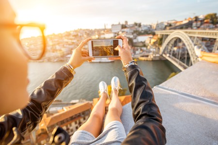 Woman photographing with phone beautiful landscape view on Porto city during the sunset in Portugalの写真素材