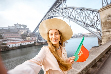 Portrait of a young woman traveler with portuguese flag on the famous iron bridge background in Porto cityの写真素材