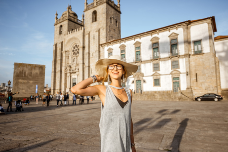 Lifestyle portrait of a young woman tourist walking on the square near the main cathedral of Porto city during the sunset in Portugalの写真素材