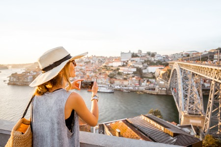 Young woman tourist photographing with phone beautiful landscape view on the old town with river and famous iron bridge in Porto city, Portugalの写真素材