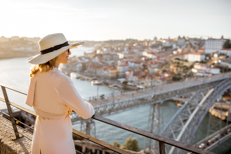 Young woman tourist enjoying beautiful aerial cityscape view with famous bridge during the sunset in Porto city, Portugalの写真素材