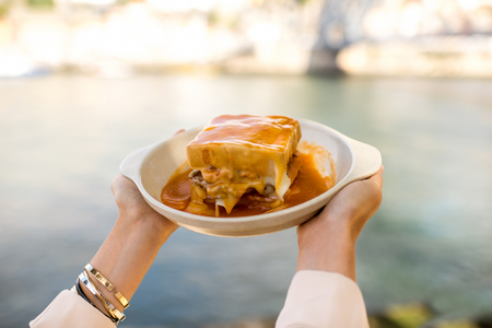 Holding a plate with traditional portuguese sandwich with meat called francesinha on the landscape background in Porto city, Portugalの写真素材