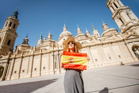 Young woman tourist standing with spanish flag in front of the famous cathedral on the central square during the sunny weather in Zaragoza city, Spainの写真素材