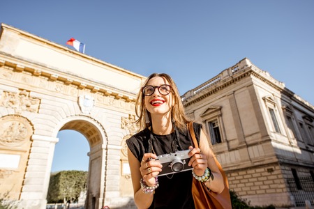 Portrait of a young happy woman tourist with photo camera in front of the famous Triumphal Arch during the morning light in Montpellier city, Franceの写真素材