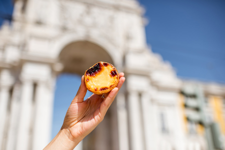Holding portuguese egg tart pastry called pastel de Nata outdoors on the triumphal arch background in Lisbonの写真素材