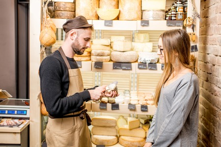 Salesman with a woman customer choosing a cheese for buying at the food storeの写真素材