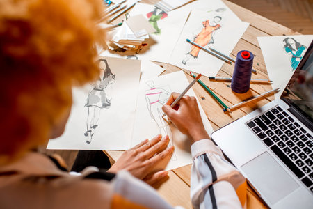 Fasion designer sketching clothes drawings at the table with tailoring tools and laptop