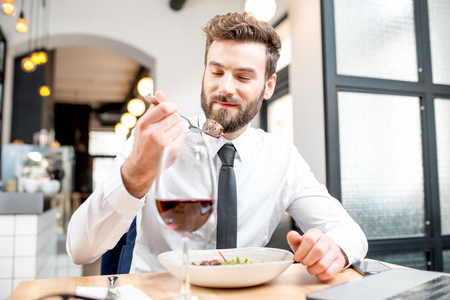 Handsome businessman in white shirt and tie having a dinner with wine and dish sitting at the restaurantの写真素材