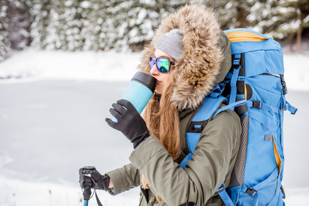 Portrait of a woman in winter clothes hiking with backpack at the snowy forest near the frozen lakeの写真素材