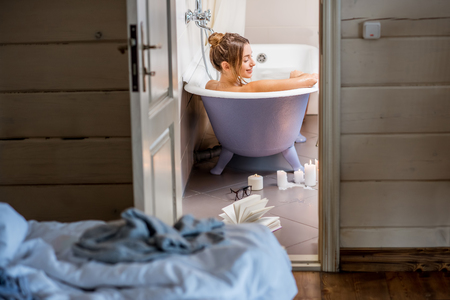 View through the bathroom door on the beautiful woman relaxing in the retro bathtub