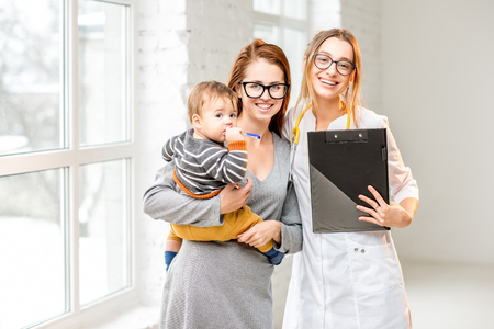 Portrait of a young woman pediatrician with mother and her baby boy at the white officeの写真素材