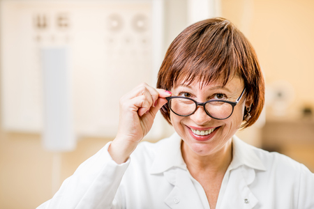 Close-up portrait of a senior woman doctor in uniform wearing eyeglasses in the ophthalmologic officeの写真素材